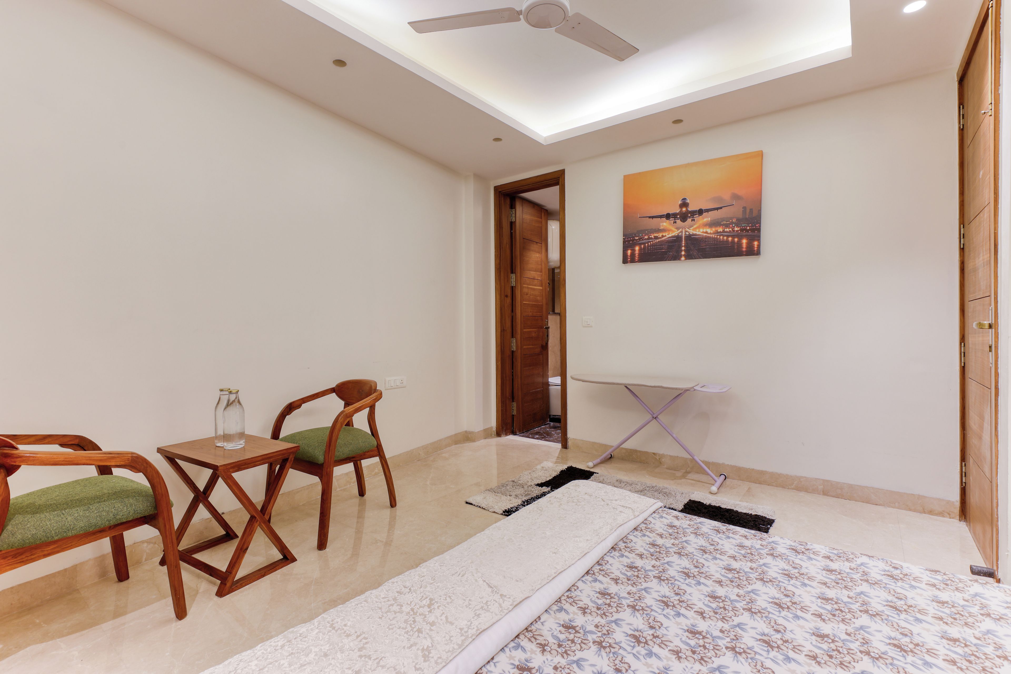 A room with a ceiling fan, a painting of an airplane, a wooden chair, a small table, and a folded blanket.
