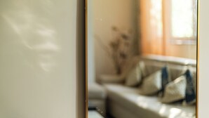 A blurred interior view of a room with a window, a sofa, and a vase with dried flowers.