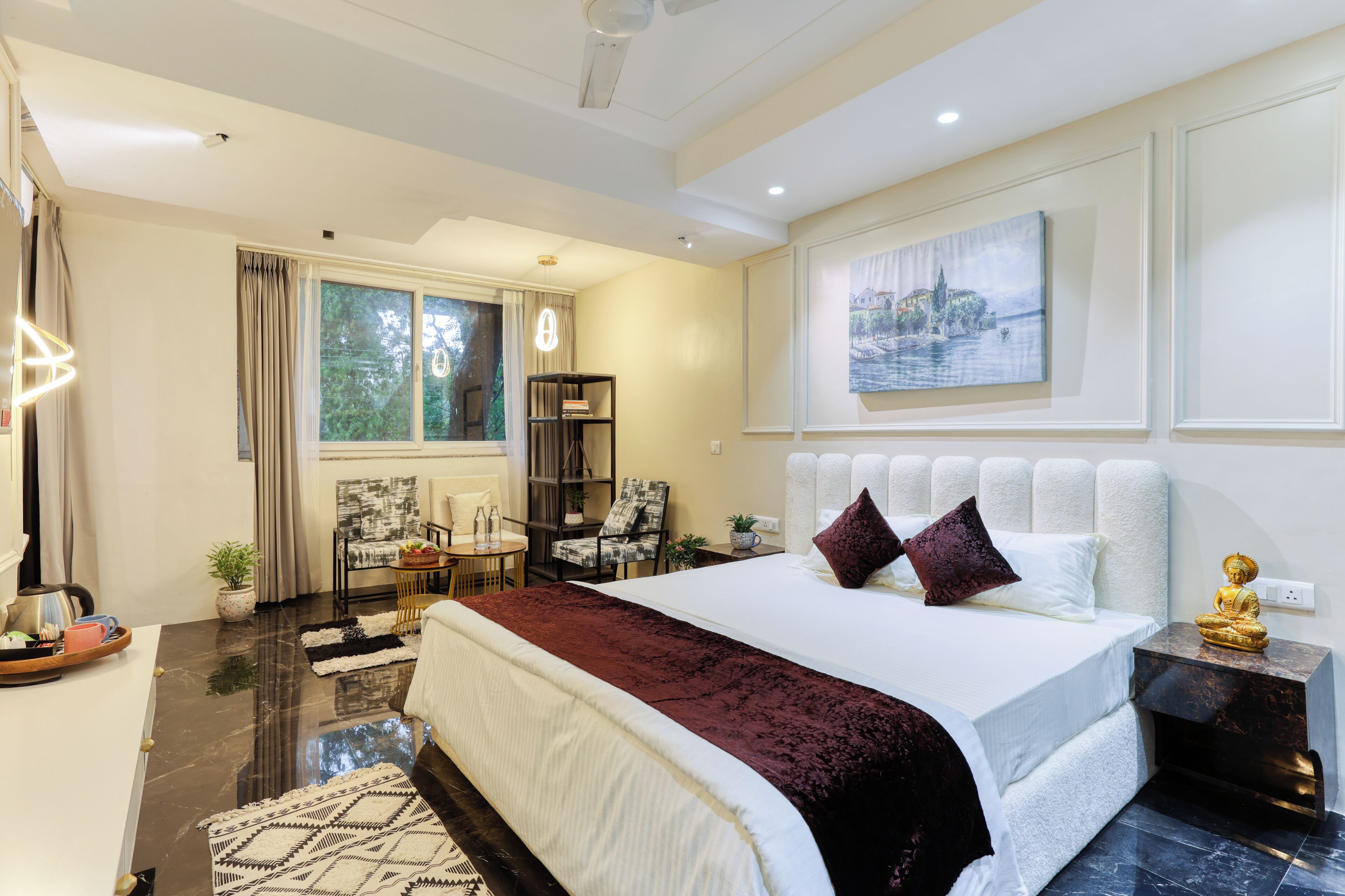 A modern bedroom with a large bed, a seating area with a table, and a view of a cityscape through the window.