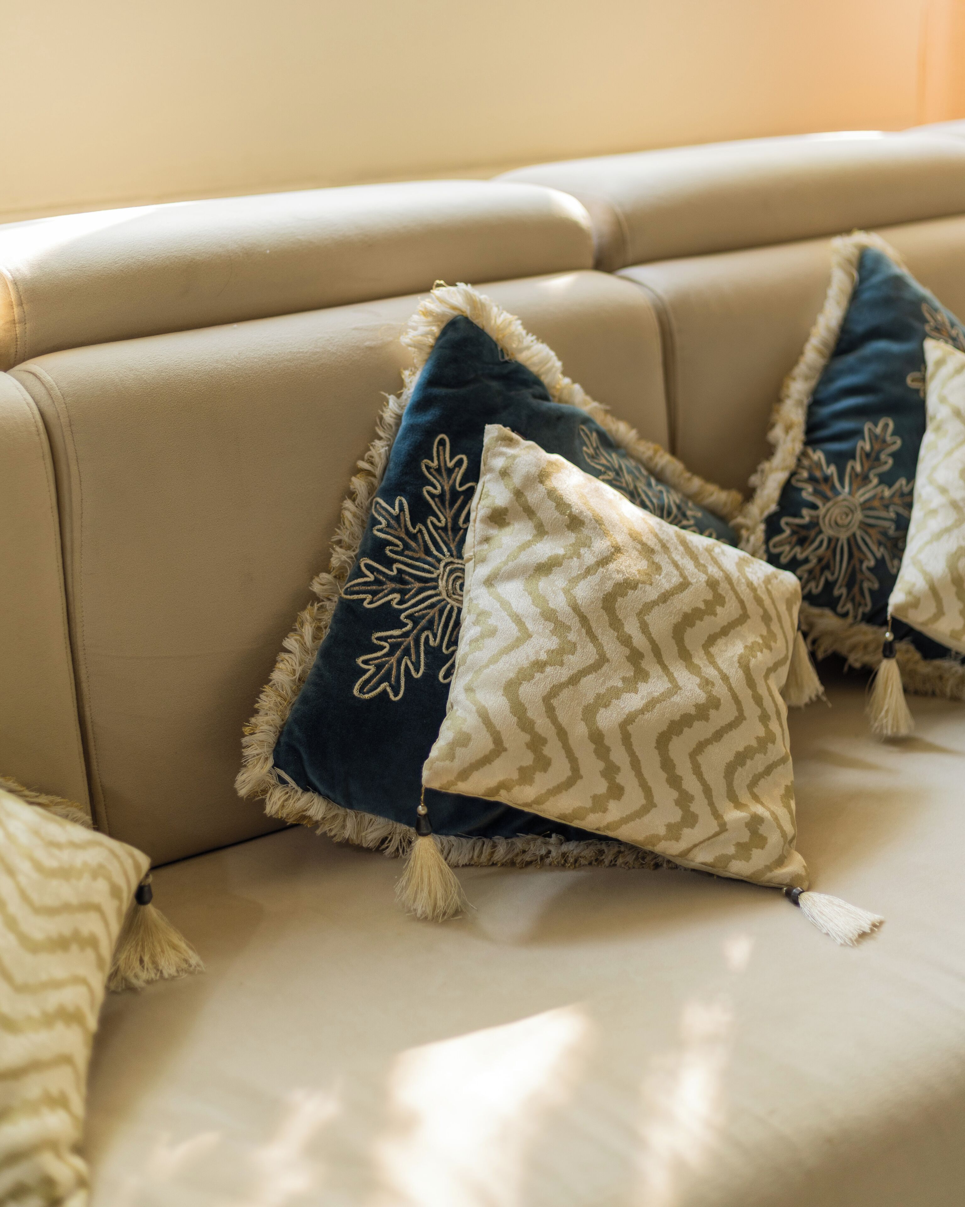 A beige sofa with decorative pillows featuring leaf and zigzag patterns.
