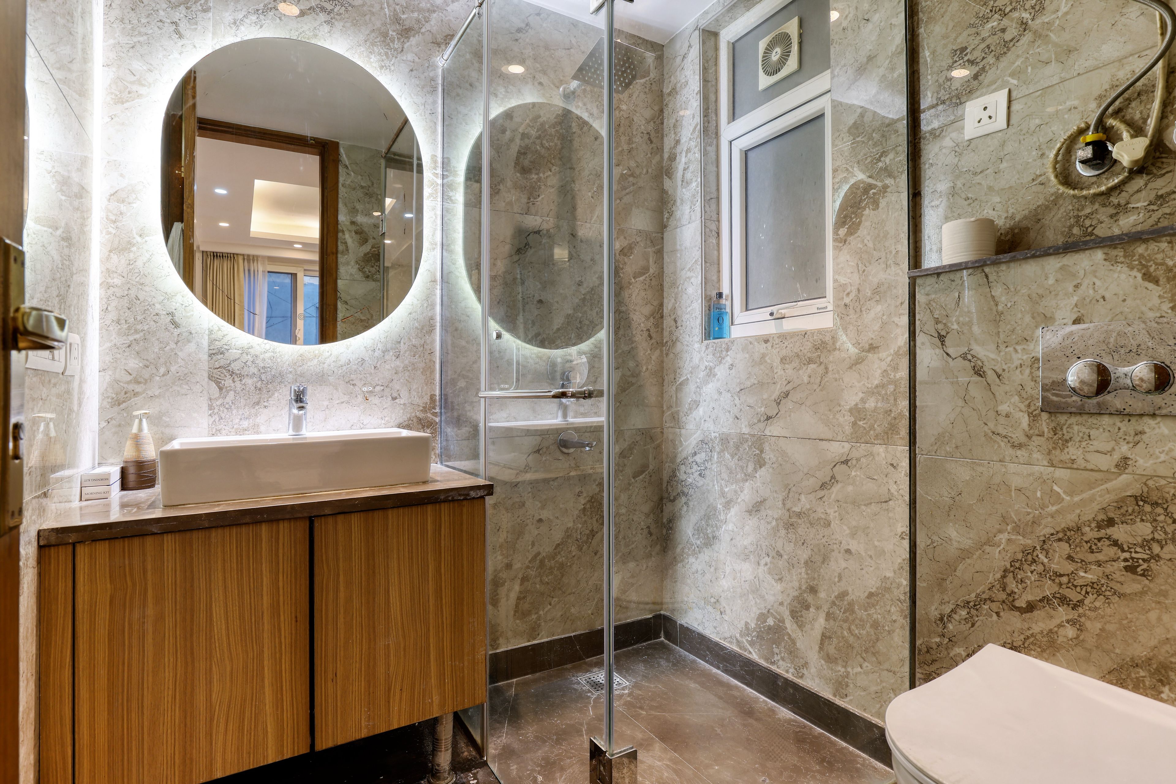 A modern bathroom with a marble sink, wooden vanity, a glass-enclosed shower, and a toilet.