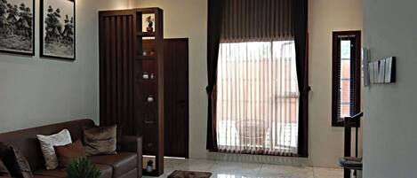 A living room with a brown sofa, a coffee table, and a large window with curtains.