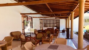 A covered outdoor seating area with wicker furniture and a tiled floor.