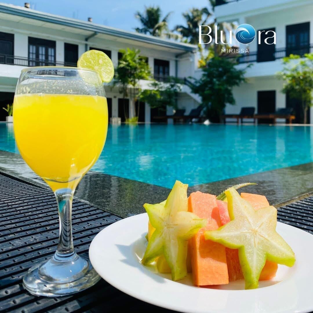 A poolside setting with a clear view of a swimming pool, a glass of yellow beverage, and a plate of fruit.