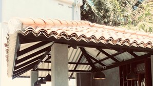An outdoor bar area with a tiled roof, concrete counter, and wooden chairs.