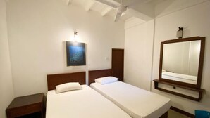 A hotel room with two single beds, a ceiling fan, a nightstand, a wall-mounted mirror, and a framed picture.