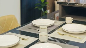 A dining table set with plates, cups, and cutlery, with a plant in the background.