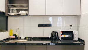 A modern kitchen with a black countertop, stainless steel cabinets, a microwave, a kettle, and a dish rack.