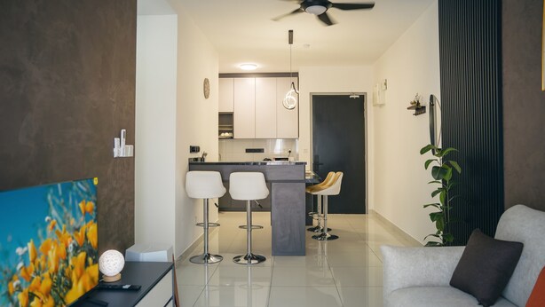 A modern living room with a sofa, a TV, and a dining area with bar stools.