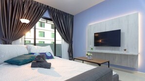 Ein modernes Hotelzimmer mit einem großen Bett, einem flachbildfernseher an der Wand, einem kleinen Tisch mit Blumen und einem Fenster mit Vorhängen.