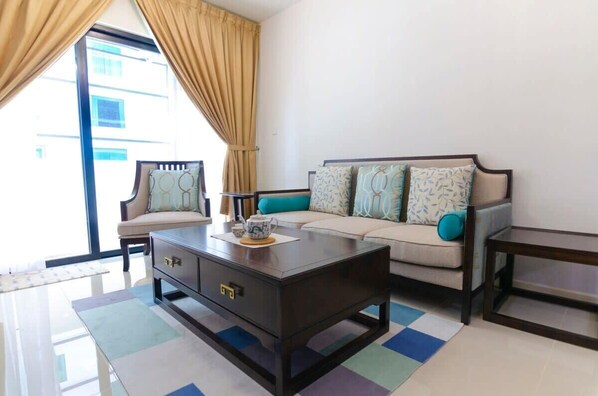 A living room with a sofa, a coffee table, and a chair. There is a window with curtains.