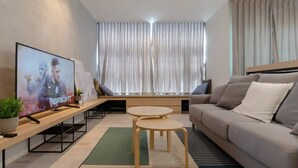 A modern living room with a sofa, two small tables, a TV, and a large window with curtains.