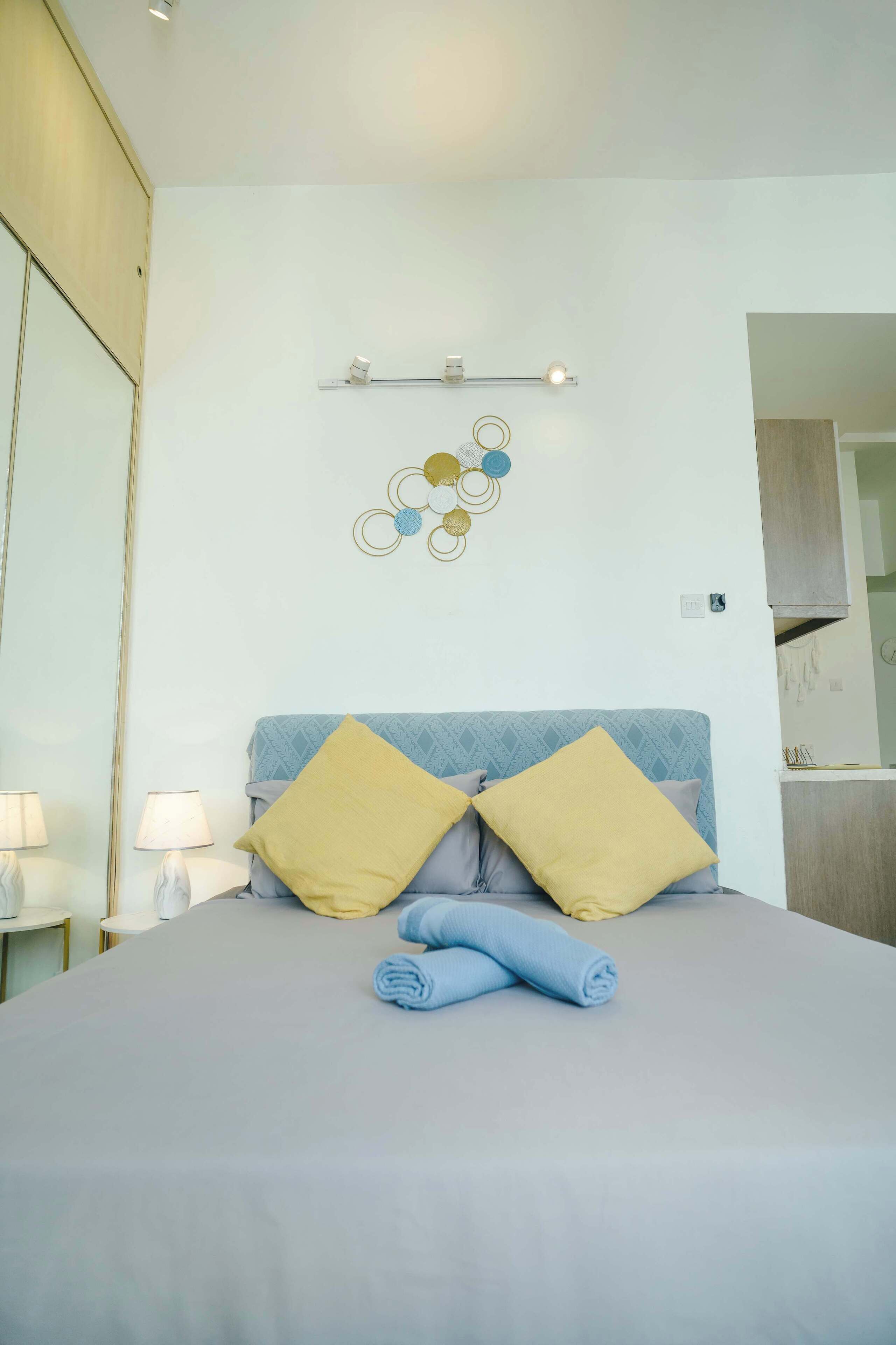 A neatly made bed with pillows, a wall-mounted light fixture, and a decorative wall piece.