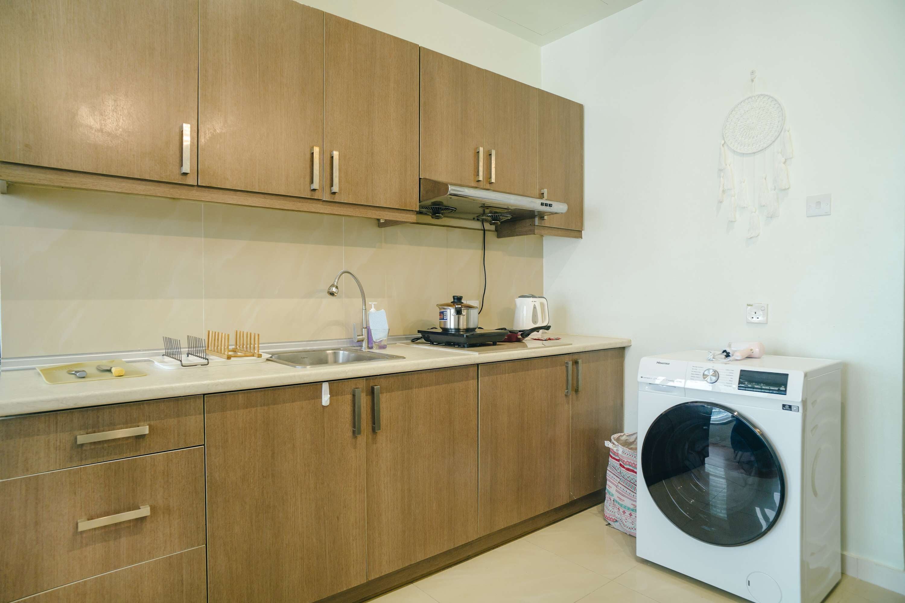 Une cuisine avec des meubles en bois, un lave-linge et un attrape-rêves accroché au mur.