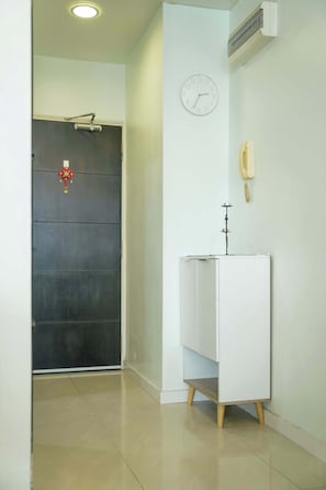 Un pasillo con una puerta cerrada, un reloj de pared, un teléfono y un armario blanco con patas de madera.