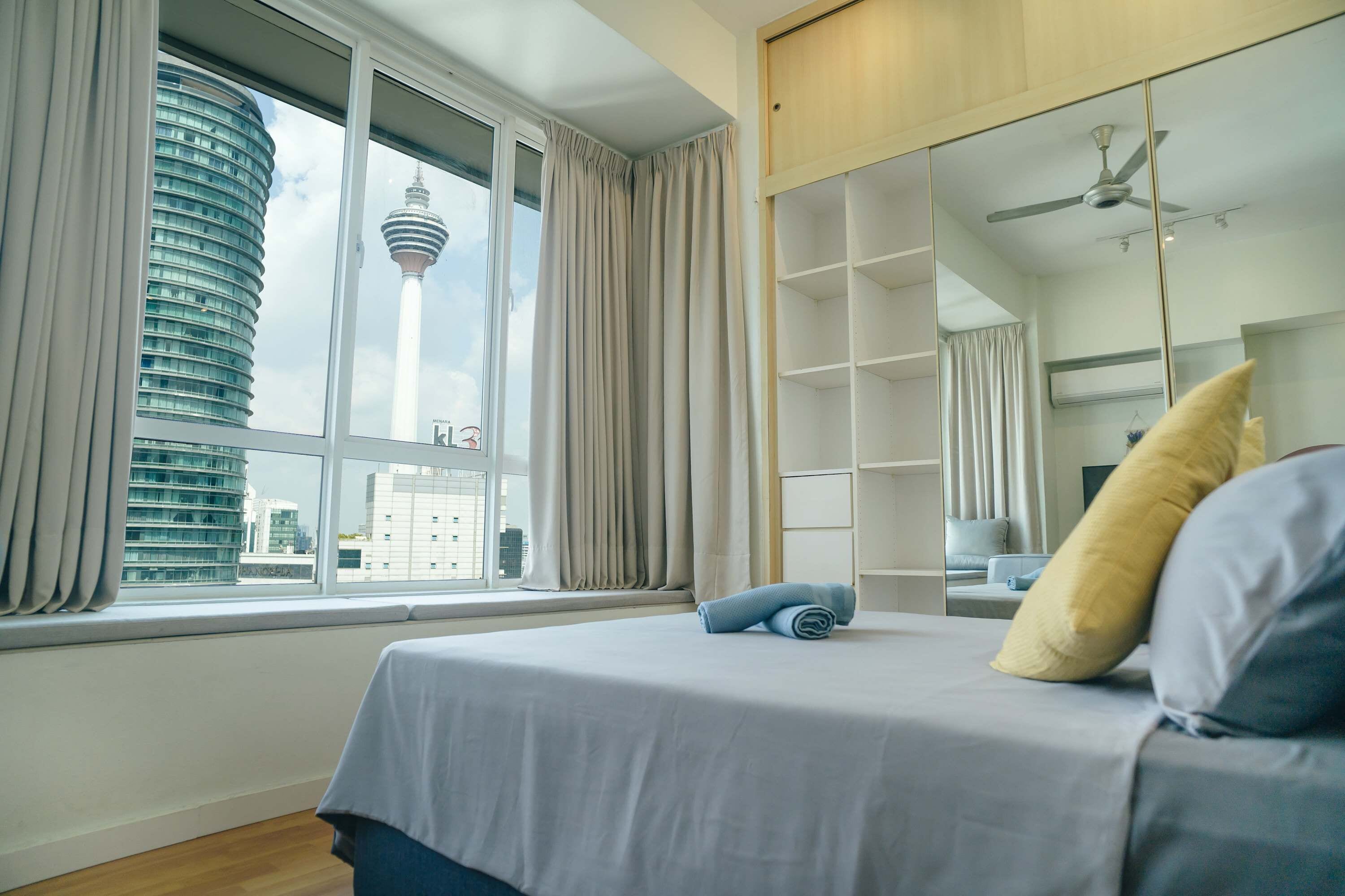 A hotel room with a bed, a large window, a wardrobe, and a view of a tower.