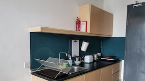 Eine kleine Küche mit schwarzer Arbeitsplatte, Holzschränken, einer abgehängten Topfhalterung, einer Feuerdecke und einem Wasserkocher.