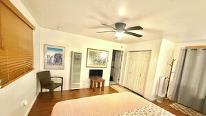 A bedroom with a bed, a ceiling fan, a chair, a TV, and a door leading to a bathroom.