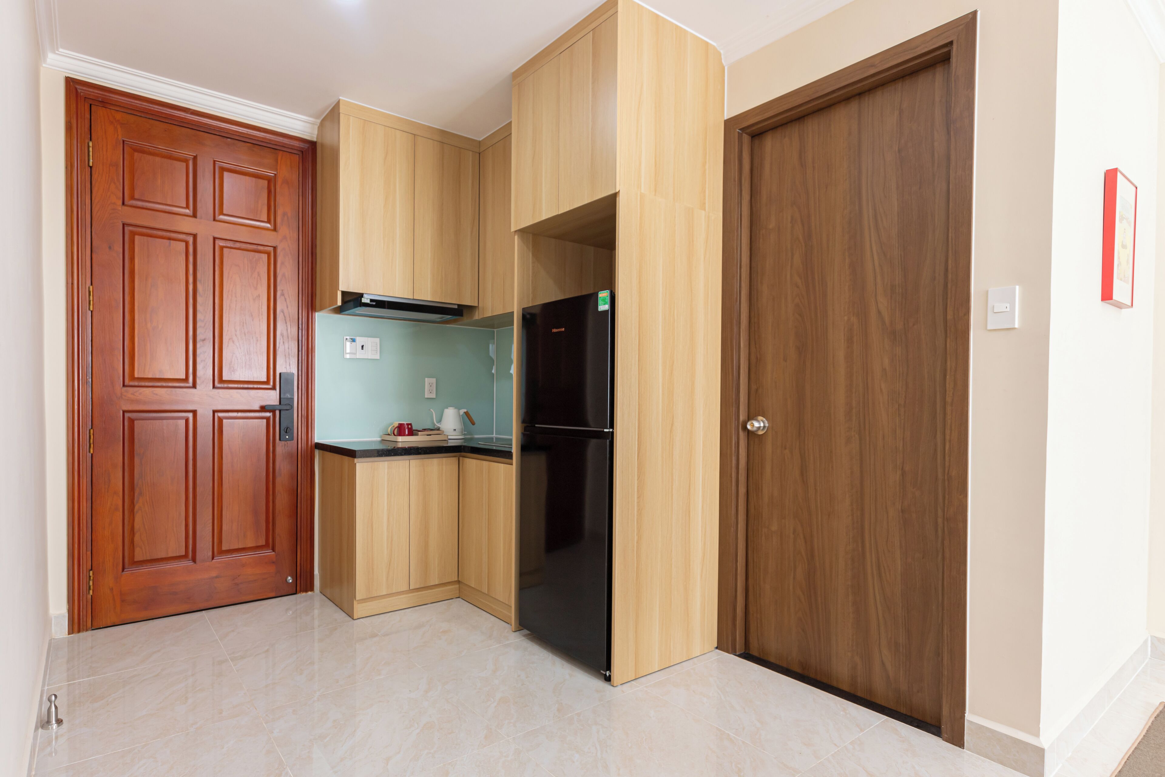 Una cocina pequeña con armarios de madera, un refrigerador negro y una puerta de madera.