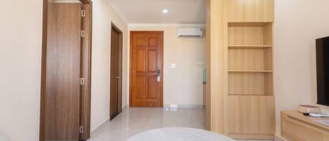 A hotel room with a large bed, a wooden wardrobe, a TV stand, and a built-in shelf unit.