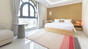 Une chambre d’hôtel moderne dotée d’un grand lit, d’une table ronde, d’un canapé et offrant une vue sur l’extérieur grâce à une grande fenêtre.