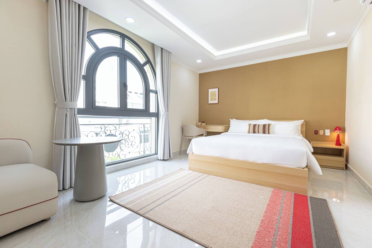 Un hotel moderno con una cama grande, una mesa redonda, un sofá y vistas al exterior a través de un ventanal amplio.