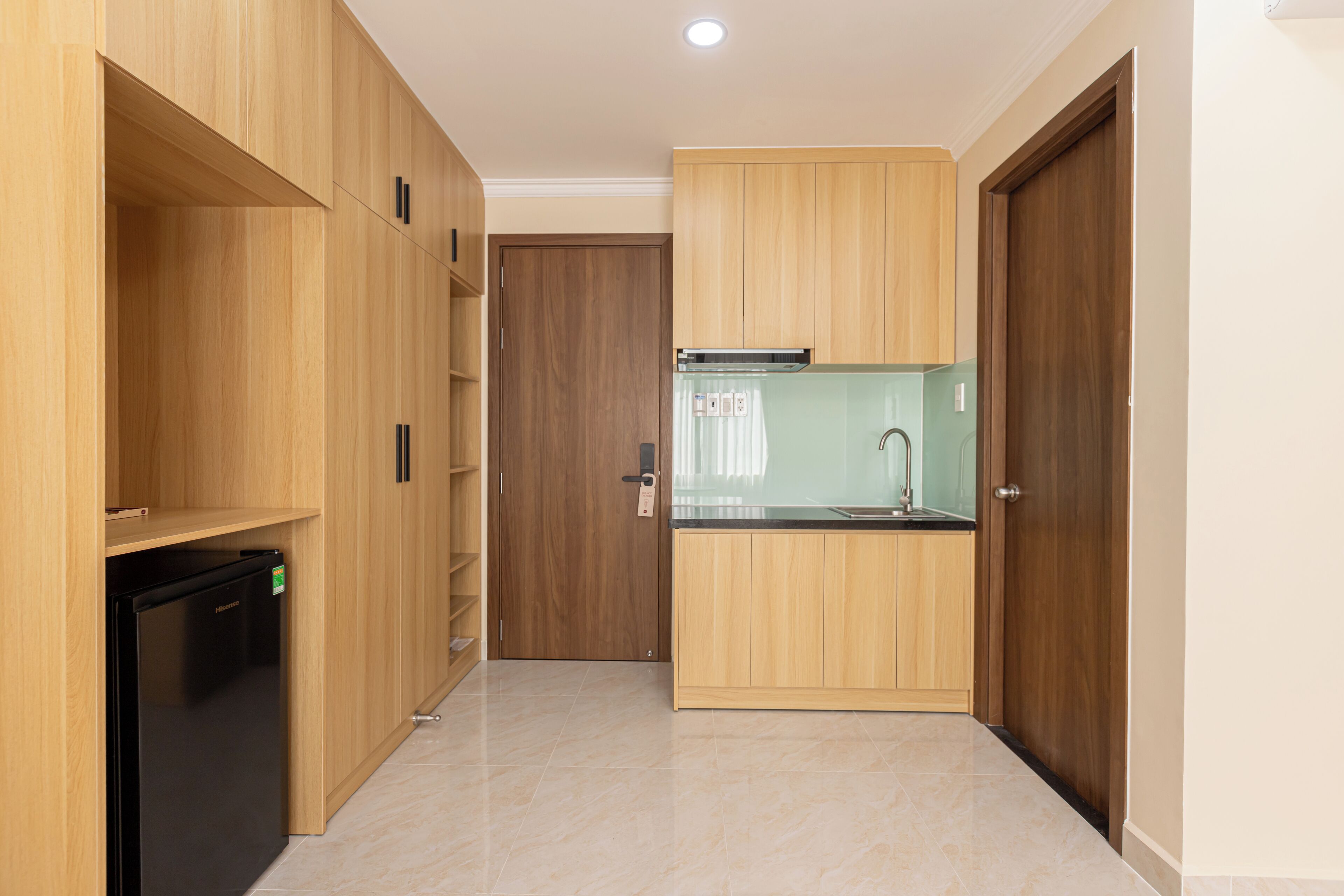 A compact kitchen with wooden cabinets, a black refrigerator, and a glass backsplash.