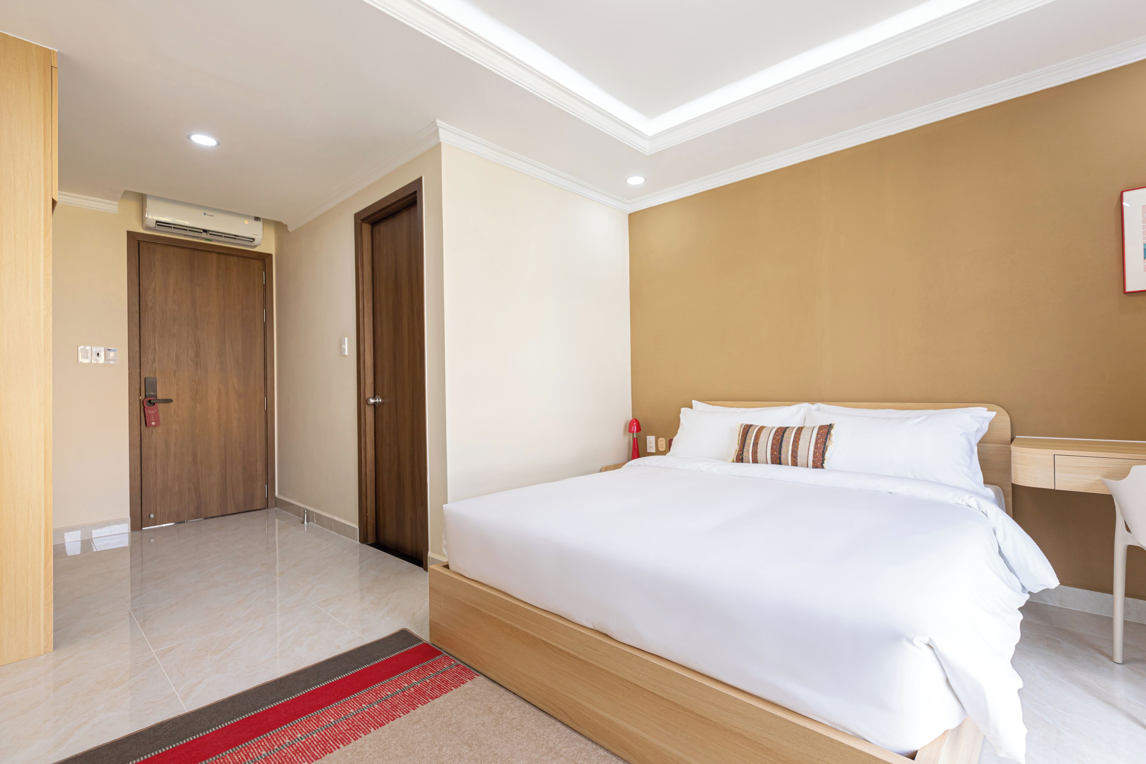 A hotel room with a large bed, a bedside table, a desk, and a red lamp.