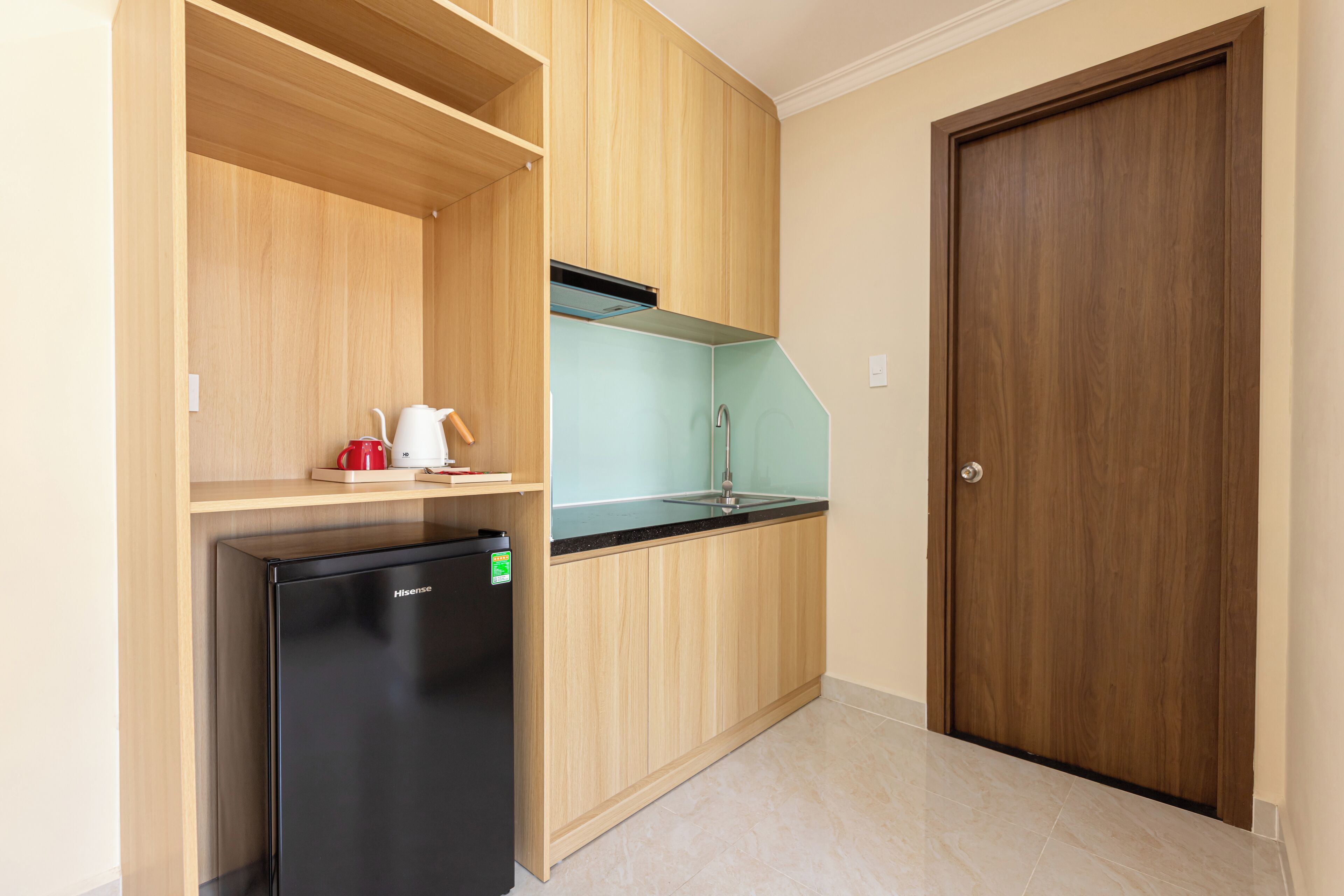A compact kitchen with a black refrigerator, wooden cabinets, a sink, and a door.