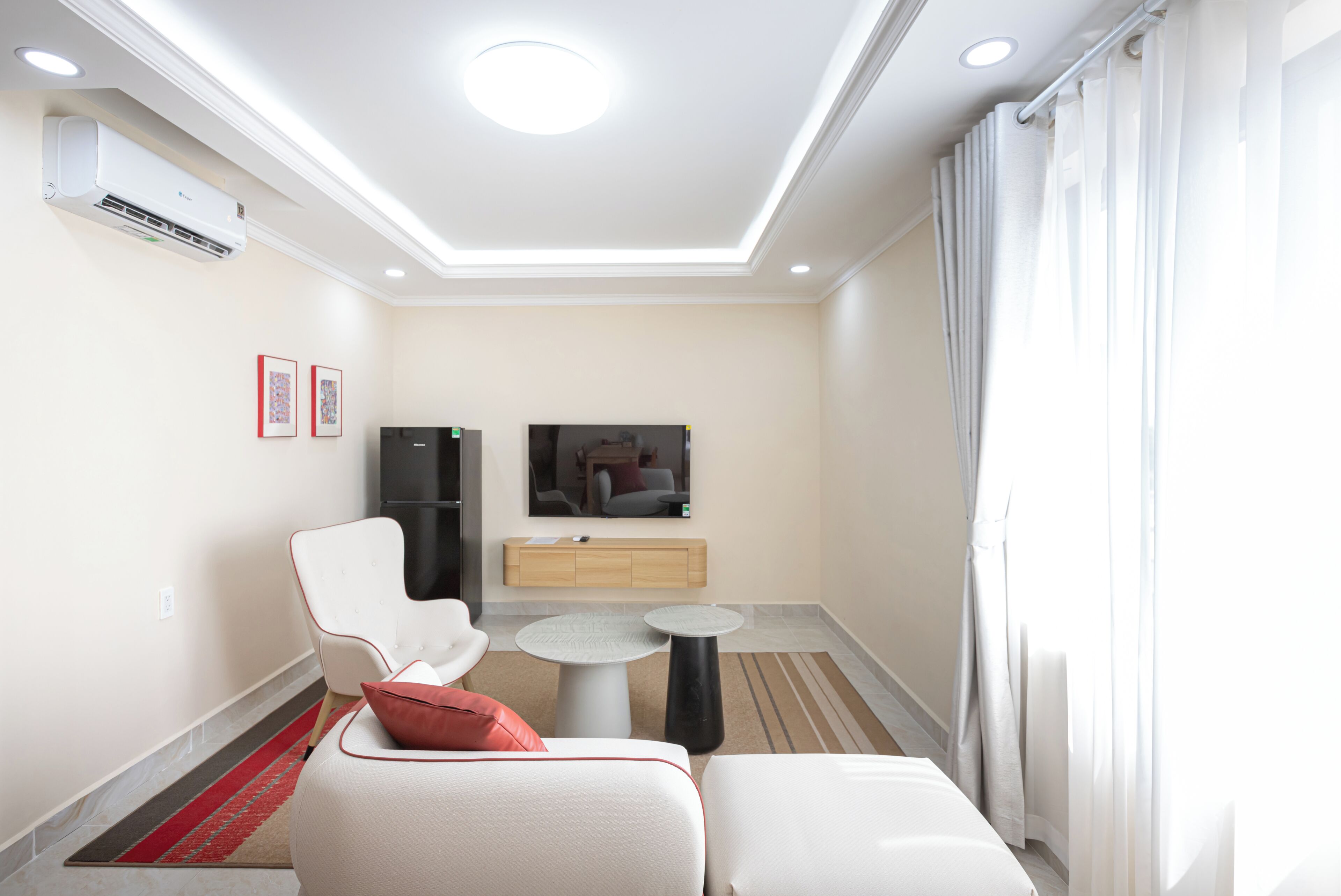 Ein modernes Hotelzimmer mit einer Couch, einem kleinen runden Tisch, einem Flachbildfernseher und einer eingebauten Klimaanlage.