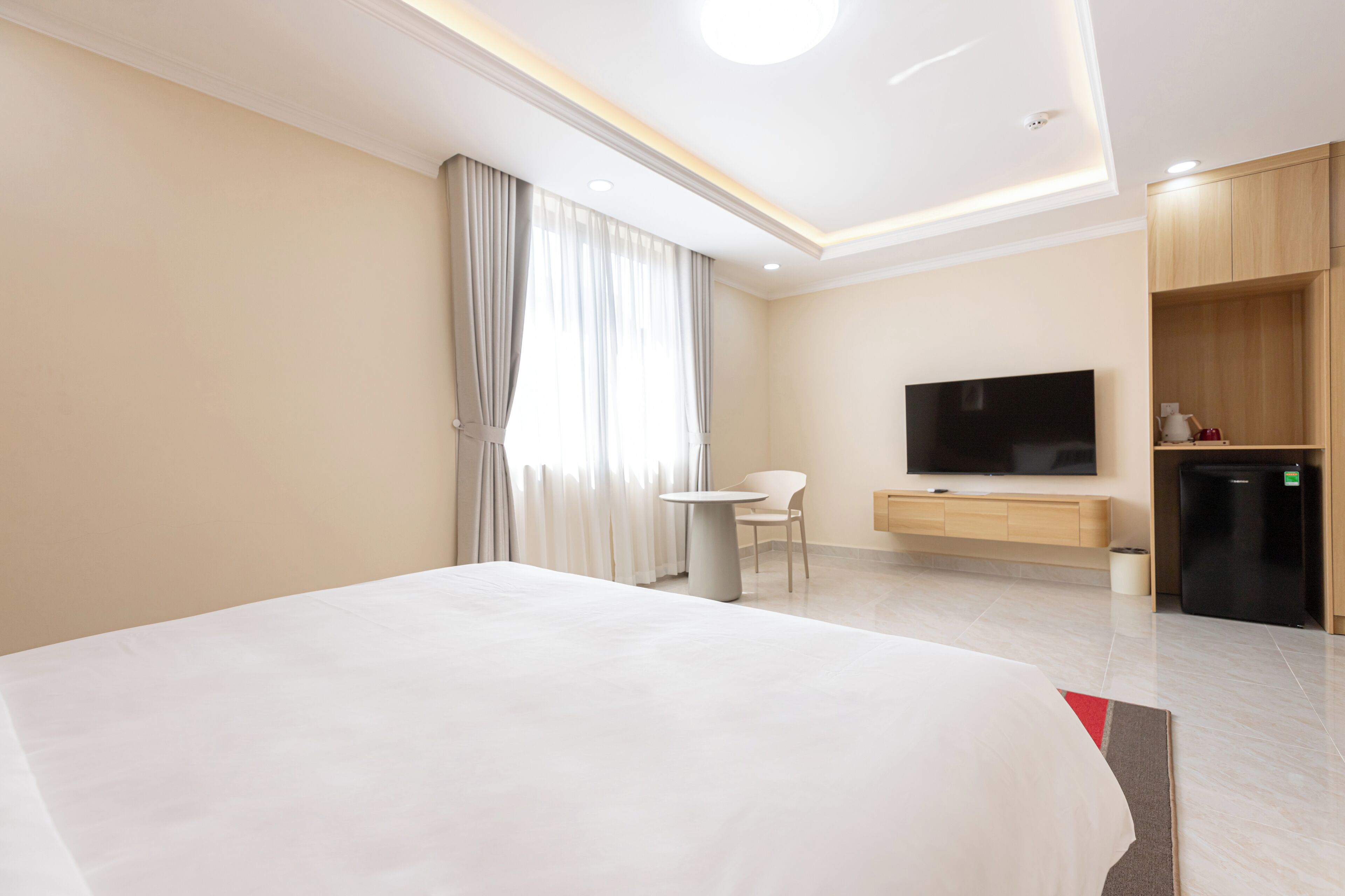 A modern hotel room with a large bed, a TV, a small table, and a desk.