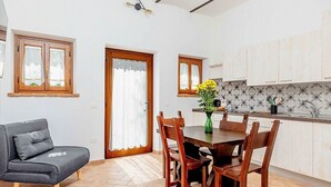 Een moderne keuken met houten kastjes, een eettafel met stoelen en een grijze bank.
