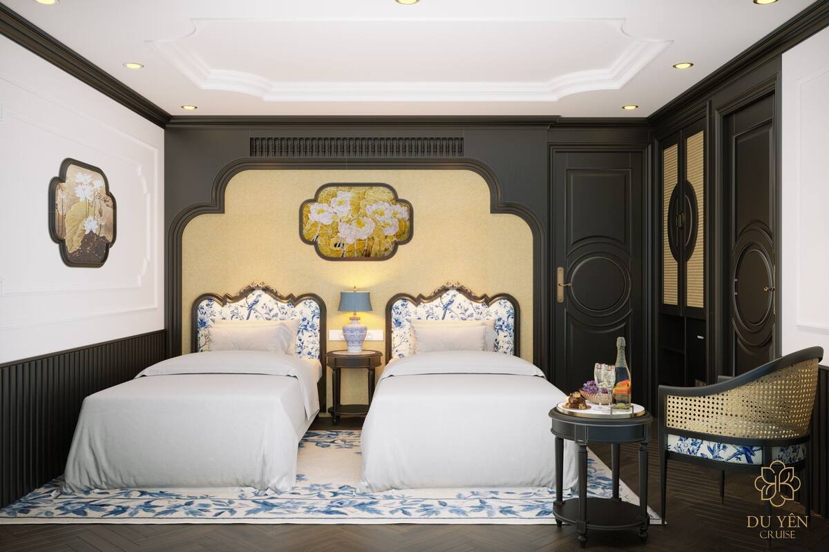 A hotel room with two beds, a small table with a lamp, a decorative wall piece, and a wicker chair.
