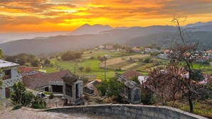 Un paysage rural avec des maisons et une montagne en arrière-plan, au coucher du soleil.
