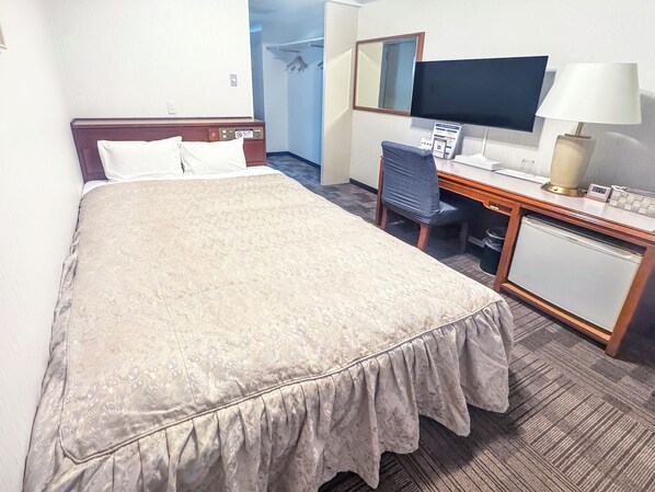 Ein Hotelzimmer mit einem großen Bett, einem Schreibtisch mit Stuhl, einem Fernseher und einer kleinen Kühlmöglichkeit.
