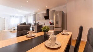 A modern living room with a wooden coffee table, two sofas, and a kitchen area with a refrigerator and cabinets.