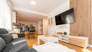 A modern living room with a grey sofa, white coffee table, and a TV mounted on a wooden wall.