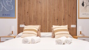 A neatly made bed with striped pillows and rolled towels, wooden paneling on the wall, and framed artwork.
