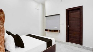 A bedroom with a bed, a wooden door, and a white wall with a mounted shelf. - Hotel River View & Restaurant (Hathras)