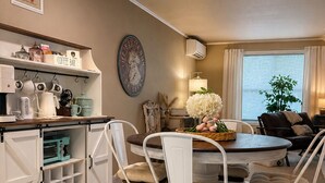 A dining area with a round table, four white chairs, a coffee bar, and a wall-mounted clock. -  Stable House INN - Pool - Horse Farm - Hot Tub - Near Smith Rocks State Park (Redmond)
