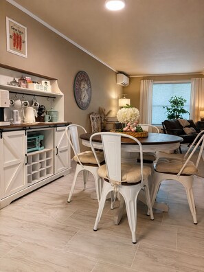 A dining area with a round table, four white chairs, a coffee bar, and a wall-mounted clock. -  Stable House INN - Pool - Horse Farm - Hot Tub - Near Smith Rocks State Park (Redmond)
