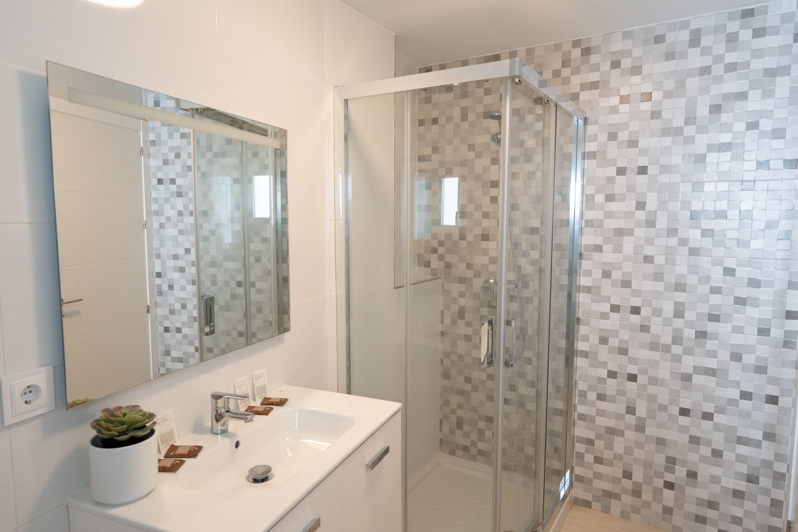 A modern bathroom with a glass shower enclosure, a white sink, and a tiled backsplash.