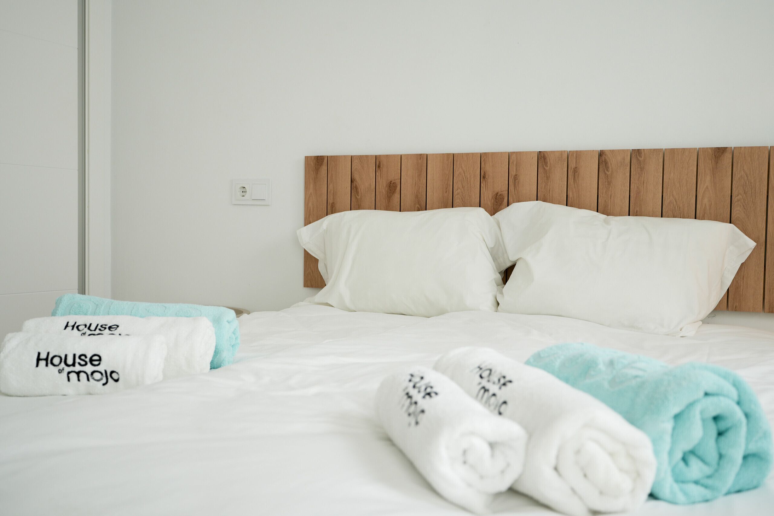 A hotel room with a wooden headboard, white bedding, and towels with 'House of Mojo' branding.