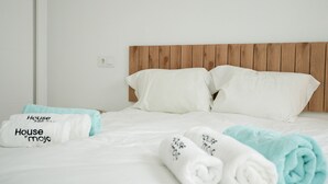 A hotel room with a wooden headboard, white bedding, and towels with 'House of Mojo' branding. - La Casita Fuengirola - Charming 3 bed ground floor (Fuengirola)