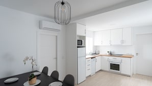 A modern kitchen with white cabinets, a microwave, and a sink. There is a dining table with plates and a potted plant. - La Casita Fuengirola - Charming 3 bed ground floor (Fuengirola)