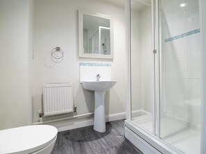 A bathroom with a toilet, a pedestal sink, a mirror, and a glass shower enclosure. - 4-Bed Home near Telford Centre (Telford and Wrekin)