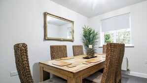 Ein Esszimmer mit Holztisch, gewobenen Stühlen, einem Spiegel und einem Fenster mit Jalousien.