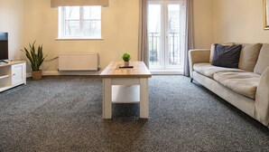 Ein Wohnzimmer mit einer Couch, einem kleinen Tisch, einer Heizung, einem Fernseher und einem Fenster mit Vorhängen.
