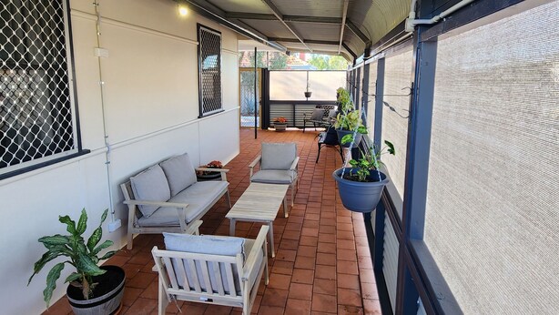 Ein überdachter Patio-Bereich mit Sitzgelegenheiten im Freien, Blumentöpfen und Blick auf die Straße.