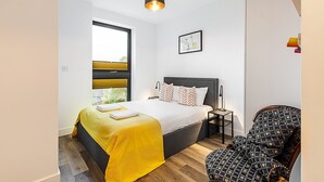 Une chambre moderne comprenant un lit, une table de chevet, une chaise et une fenêtre avec des stores.